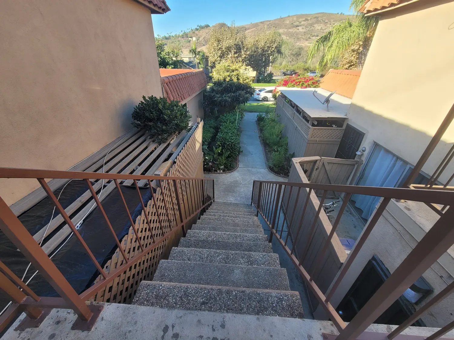 Exterior concrete stairs running down between two tile-roofed community buildings, with landscaping and a tarped work area