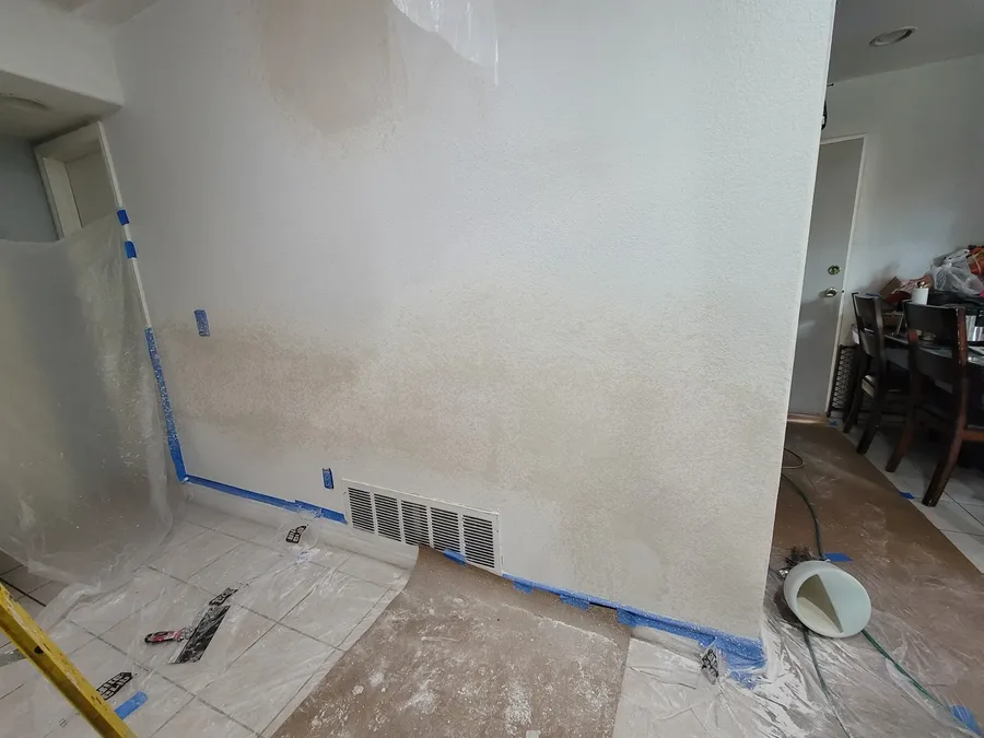 Interior wall with a large drywall patch feathered and textured to match the wall around it, taping tools on the covered floor