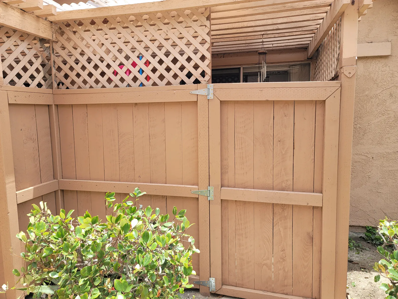 Freshly stained wood fence and matching gate with new galvanized hinges, and a diagonal lattice screen running along the top