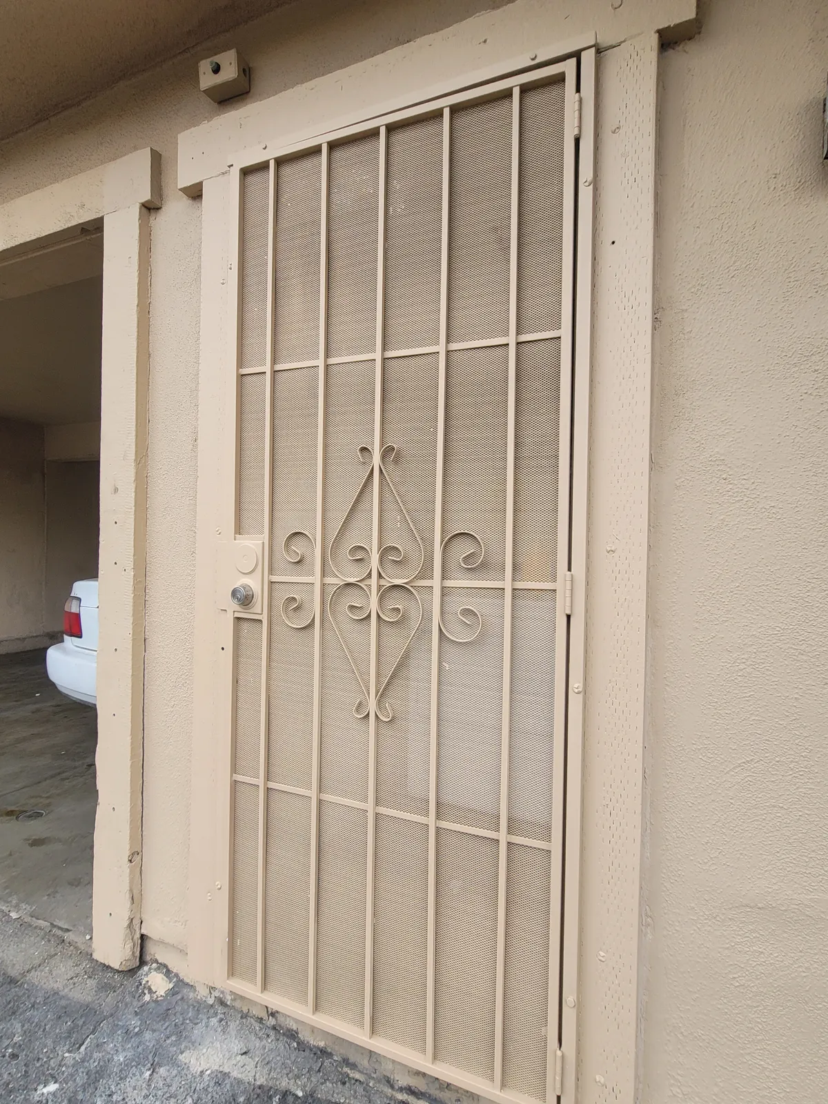 Wrought iron security screen door with a scrollwork center panel, repainted cream to match the door frame and the stucco wall around it