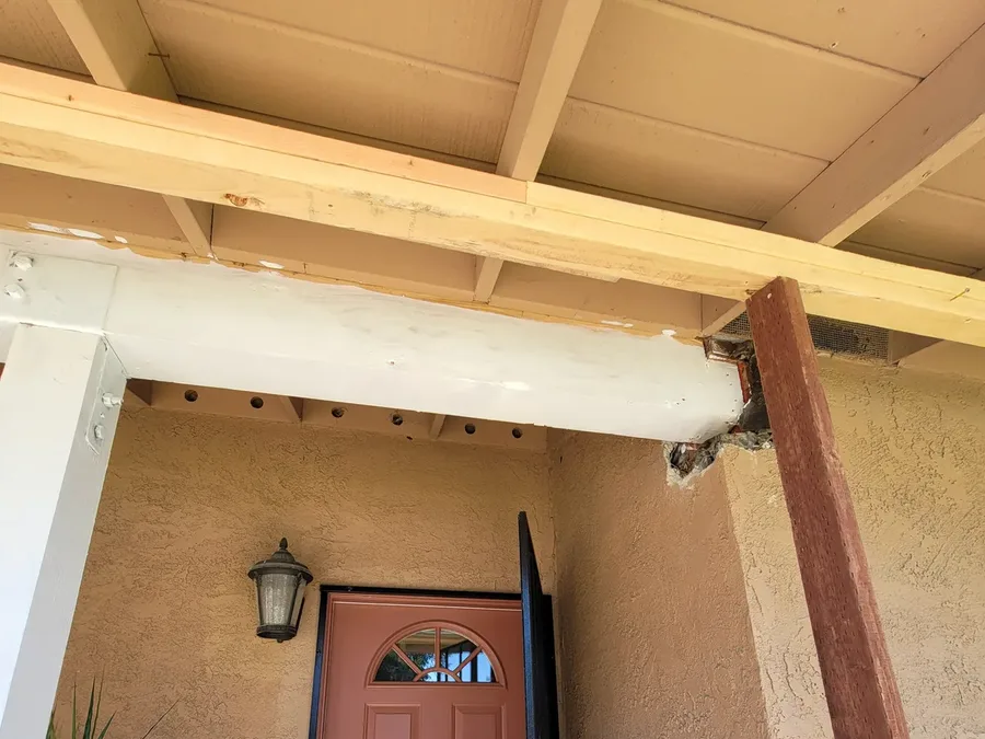 Entry porch seen from below, with a painted beam whose end is split and deteriorated where it meets the post