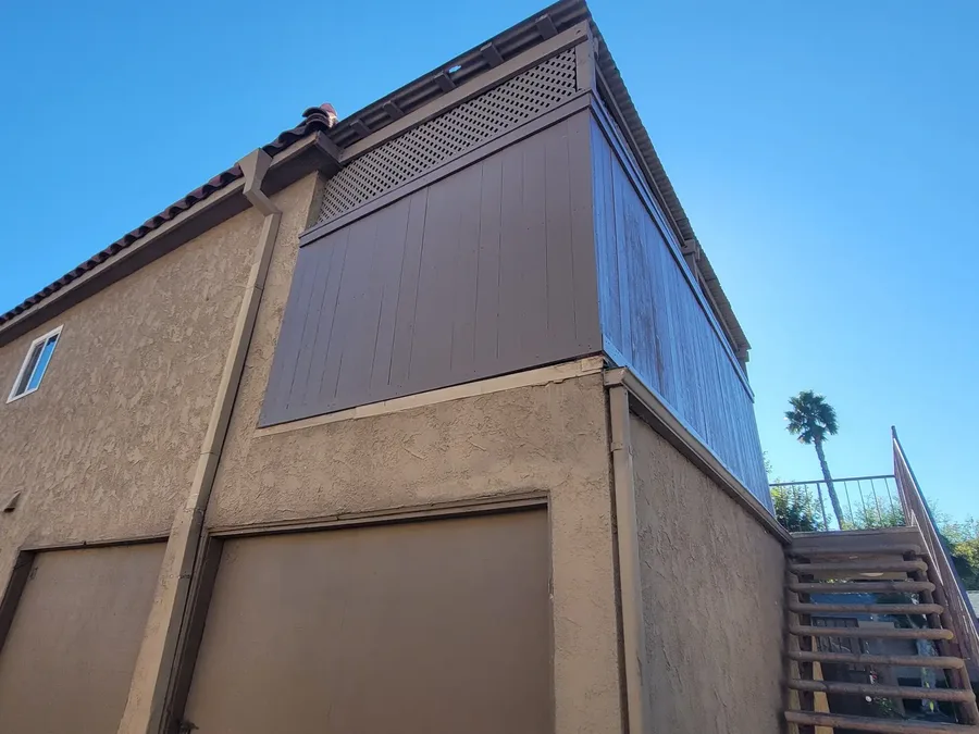 Wood board and lattice screen wall where the left panel is freshly painted brown and the right panel is still weathered grey