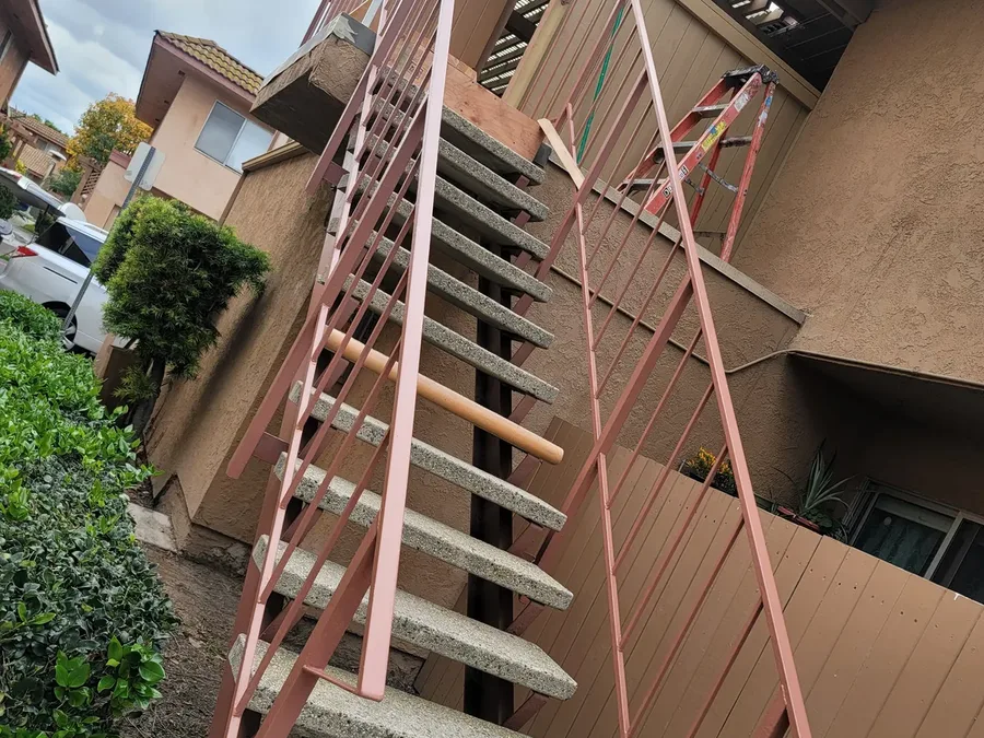 Exterior stairway at a community building with concrete treads and a steel stringer and railing coated in red oxide primer