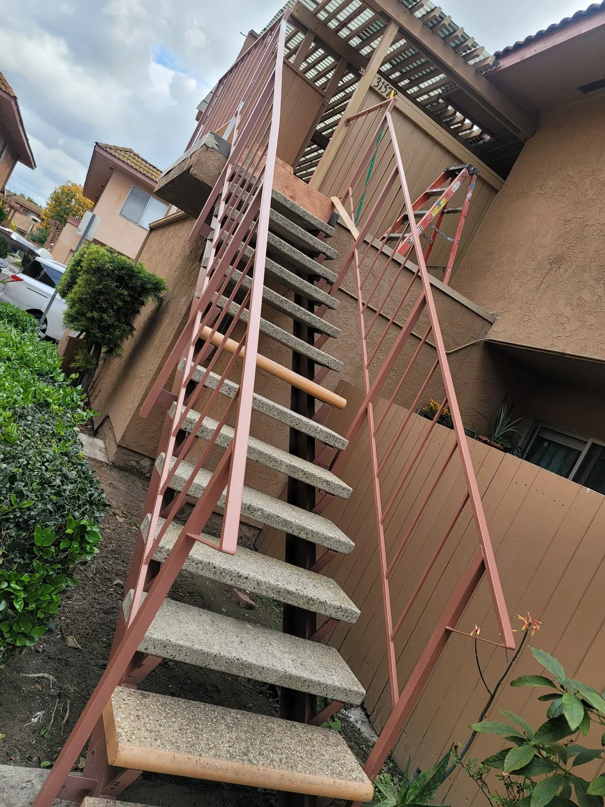 Exterior stairway at a community building shot from the bottom, with concrete treads and a steel stringer and railing coated in red oxide primer