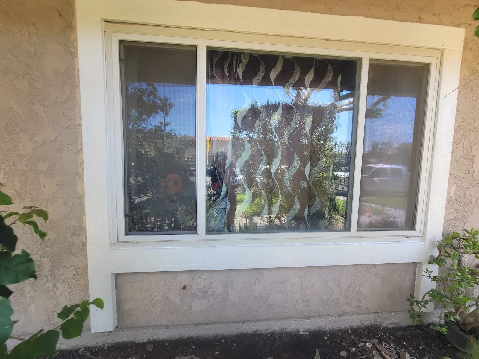 Exterior sliding window in a stucco wall, with a fresh stucco patch across the panel below the sill and freshly painted white trim