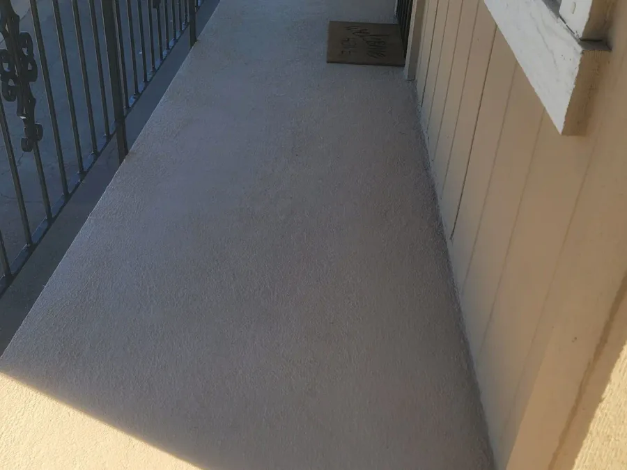 Freshly coated grey walkway deck running along a condo building, with a black metal railing on the left